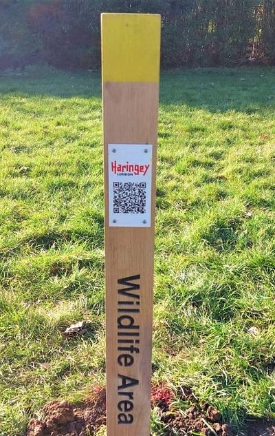 Wooden sign with yellow top in the ground saying wildflower area.