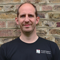 Man standing in front of brick wall wearing Haringey Music Service t-shirt.