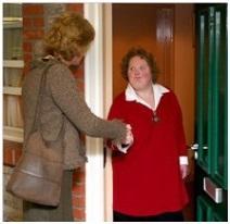 A woman greeting another woman at their front door