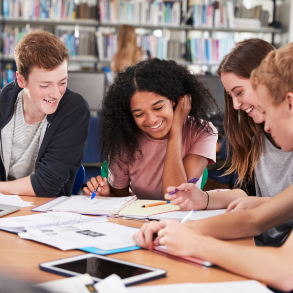 four students working at a table and smiling