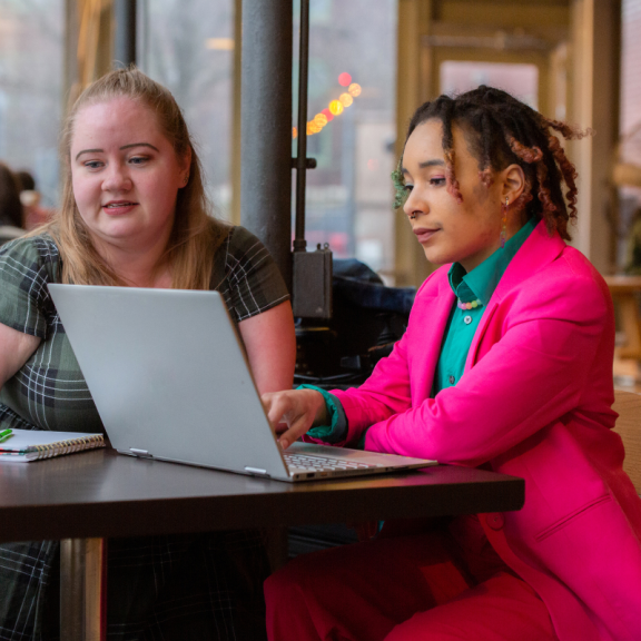 Two young adults sitting at a table looking at a computer