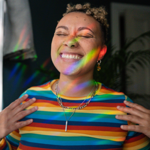 Young person with short hair and a rainbow shirt smiling