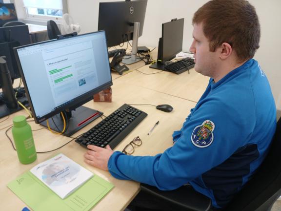 young adult sitting at a desk in front of a computer in an office setting