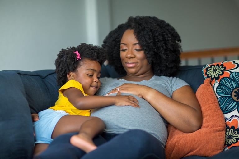 A little girl holding her mother's stomach.