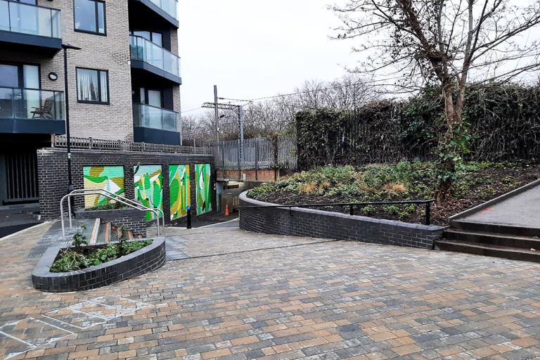 A paved pedestrian walkway with a wall of murals in shades of green