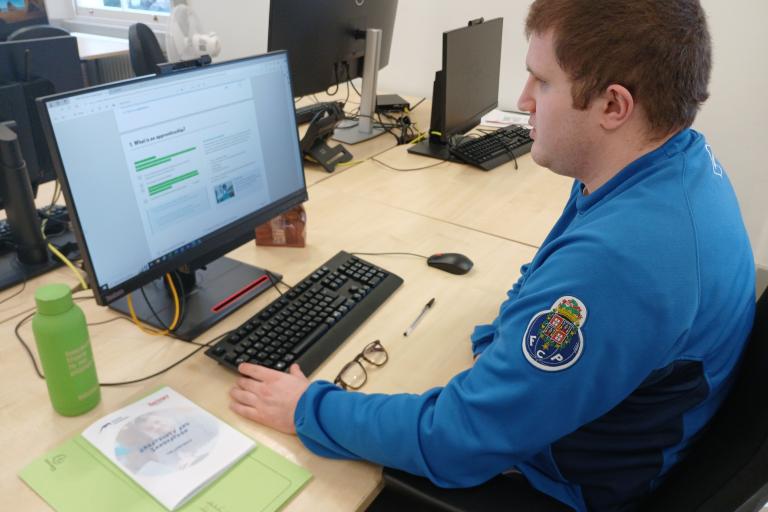 young adult sitting at a desk in front of a computer in an office setting