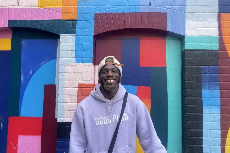 young adult smiling in front of a colourful painted wall