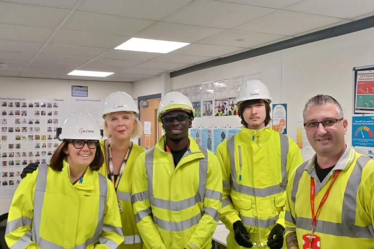 5 people in construction clothing and hard hats in an office setting