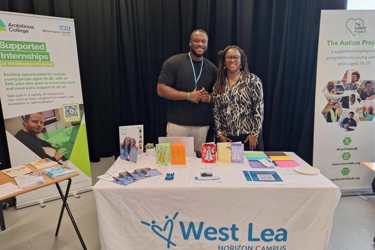 Two adults standing at a booth for West Lea and smiling at the camera