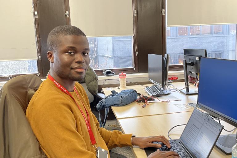 young adult sitting at a desk working on a laptop in an office setting. 