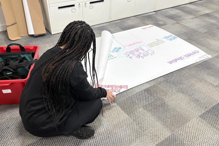young person with long hair sitting on the floor with paper