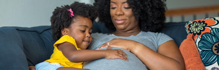 A little girl holding her mother's stomach.