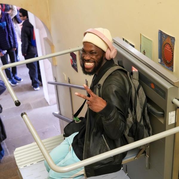 young person smiling with a peace sign sitting on a stairlift