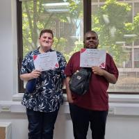 Two young adults smiling and holding certificates