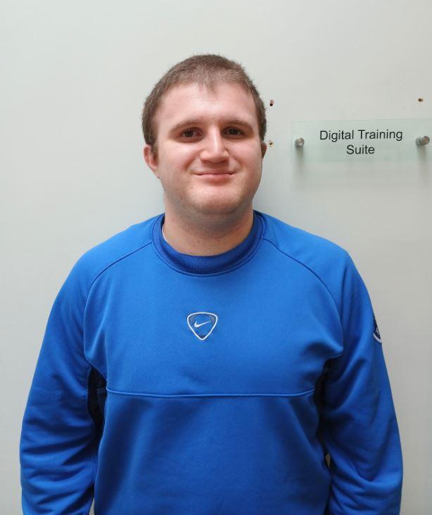 Image of a young person smiling next to a sign with the text: Digital Training Suite