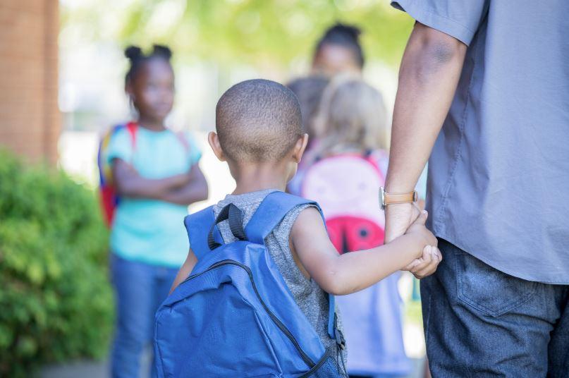 young child with a backpack holding their parents hand in a school setting