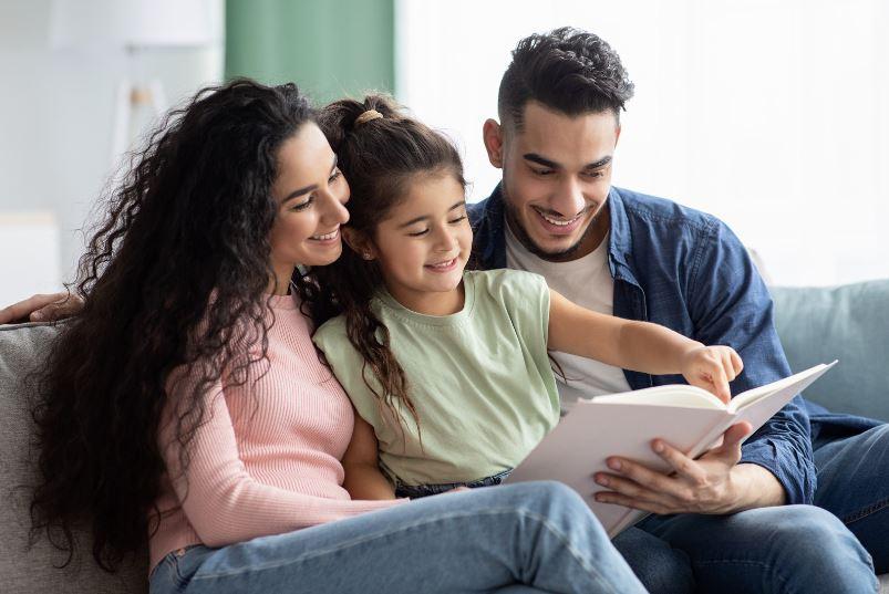 image of young child with their parents reading a book and smiling
