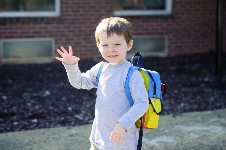 image of young child wearing a backpack and waving goodbye