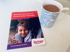 A copy of the 'Benefits and Perks of Fostering for Haringey' booklet on a kitchen worktop, next to a cup of tea